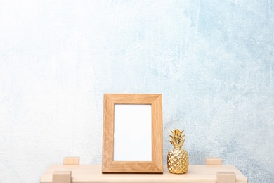 Blank frame and decorative pineapple figure on table near light wall. Mock up for design