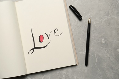 Open notebook with handwritten word Love near pen on light grey table, flat lay