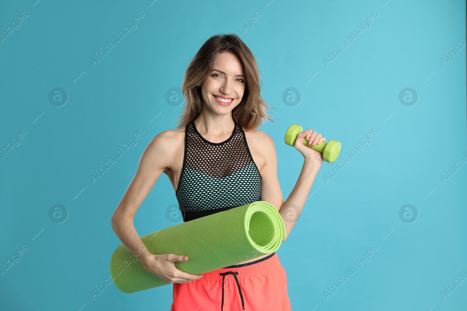 Photo of Beautiful woman with yoga mat and dumbbell on turquoise background