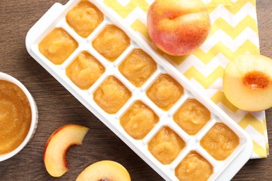 Photo of Nectarine puree in ice cube tray and fresh nectarine fruits on wooden table, flat lay. Ready for freezing