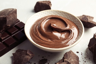 Bowl with tasty melted chocolate and pieces on table