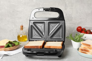 Photo of Modern sandwich maker with bread slices and different products on light grey table