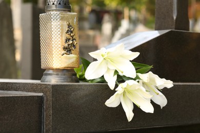 Photo of White lilies and grave light on grey granite tombstone outdoors. Funeral ceremony