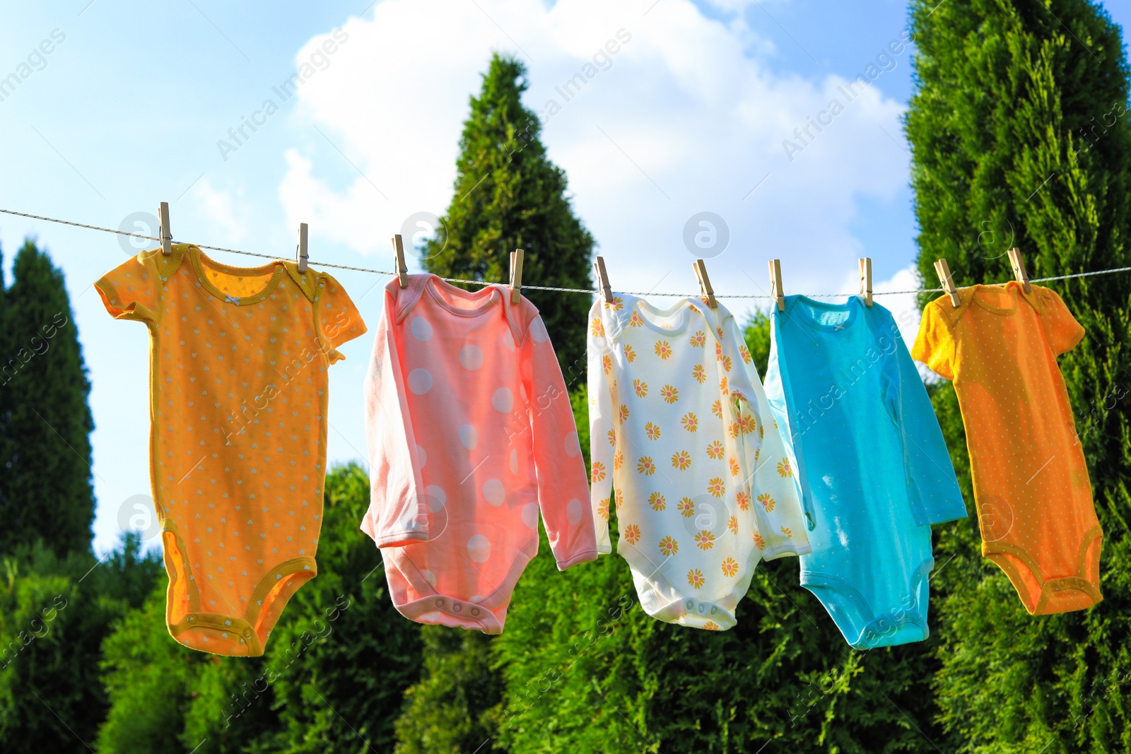 Photo of Clean baby onesies hanging on washing line in garden. Drying clothes