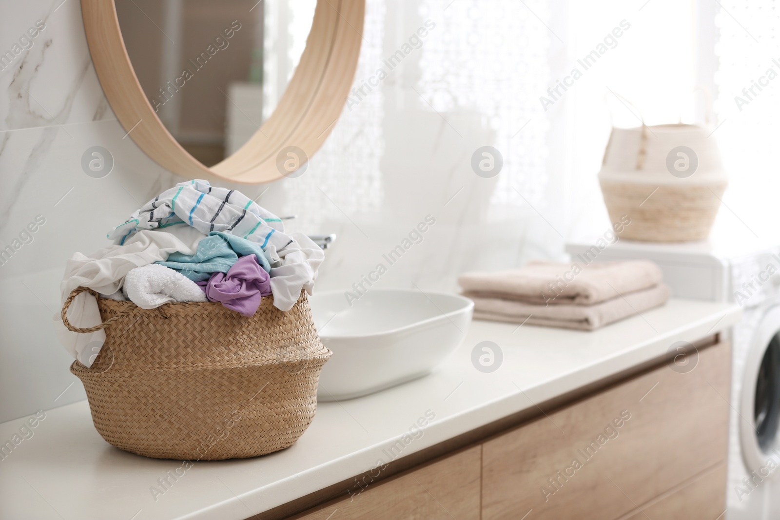 Photo of Wicker basket with dirty clothes on countertop in bathroom. Space for text