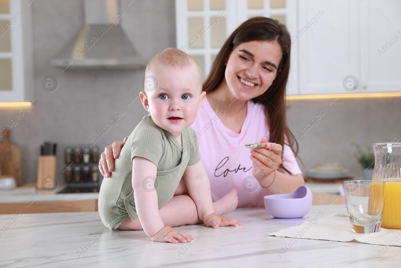 Photo of Happy young woman feeding her cute little baby at table in kitchen