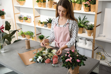 Photo of Florist making bouquet with fresh flowers at table in shop