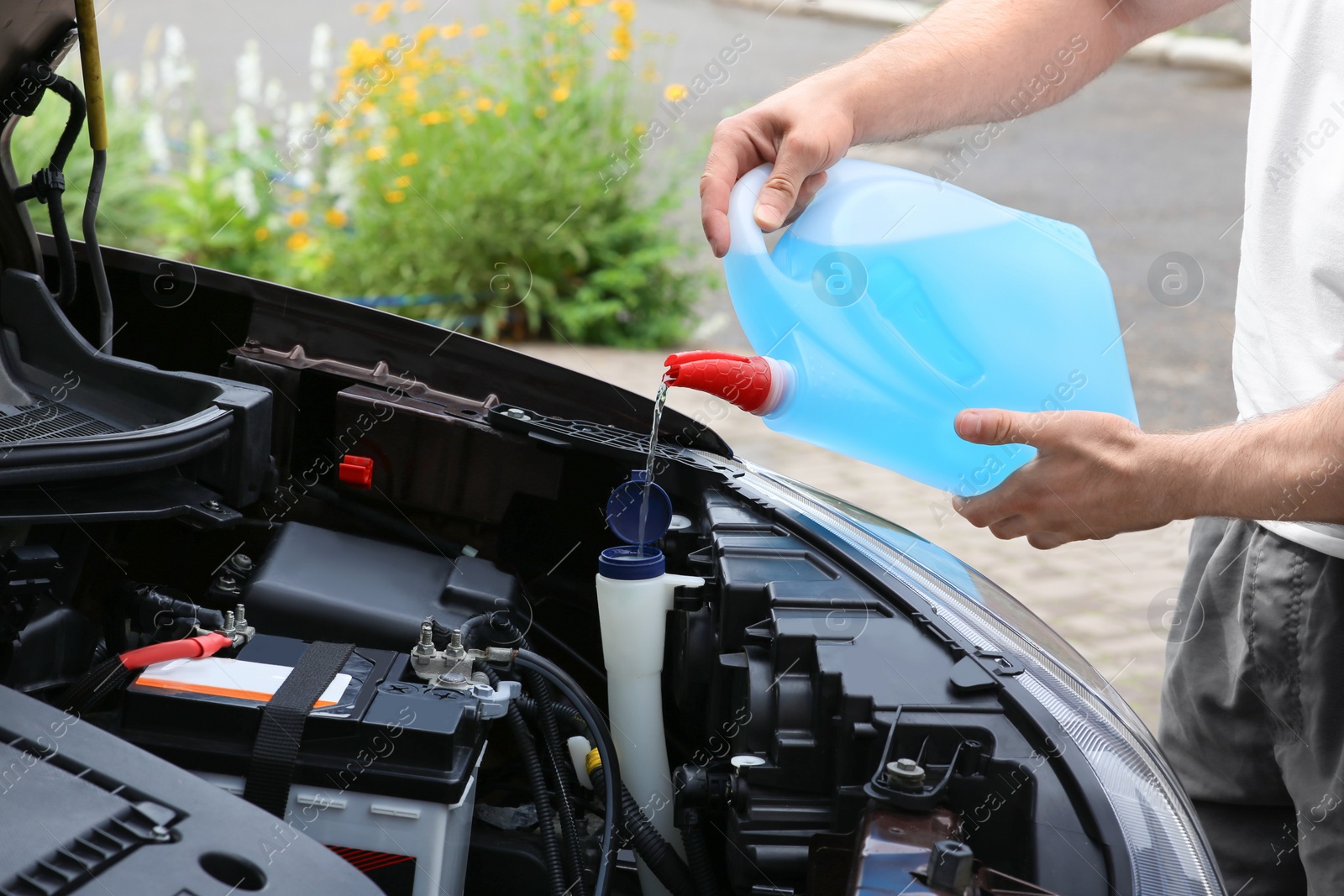 Photo of Man pouring liquid from plastic canister into car washer fluid reservoir, closeup