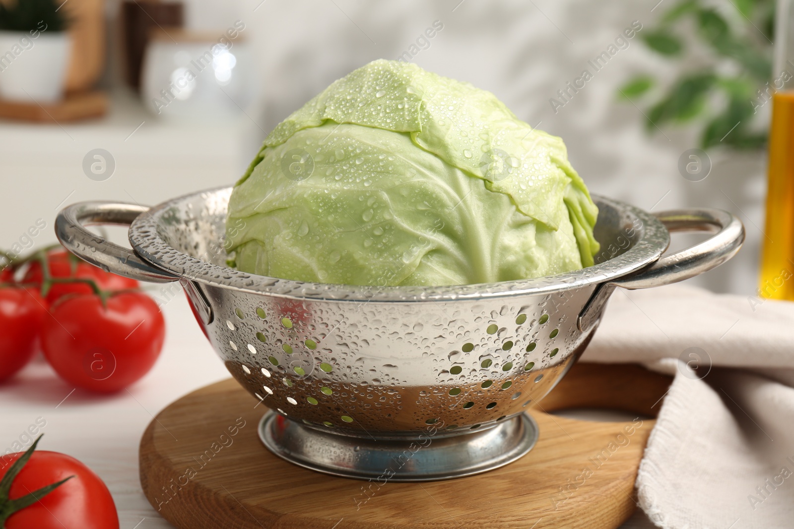 Photo of Wet cabbage in colander and tomatoes on white table, closeup