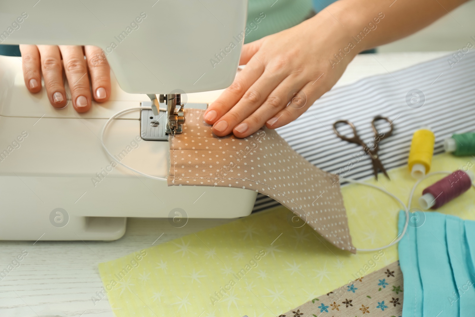 Photo of Woman sewing cloth mask with machine at table, closeup. Personal protective equipment during COVID-19 pandemic