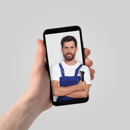 Image of Find plumber. Man using mobile phone on light grey background, closeup. Specialist looking out of gadget