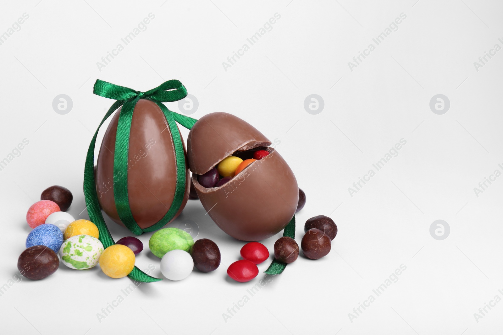 Photo of Tasty chocolate eggs and colorful candies on light background, space for text