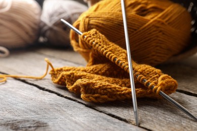 Photo of Soft orange knitting, yarns and metal needles on wooden table, closeup