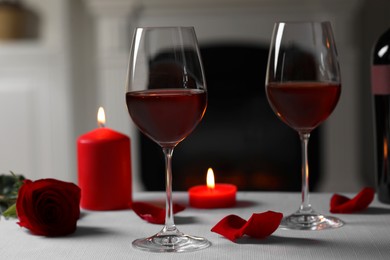 Glasses of red wine, burning candles and rose flower on grey table indoors. Romantic atmosphere