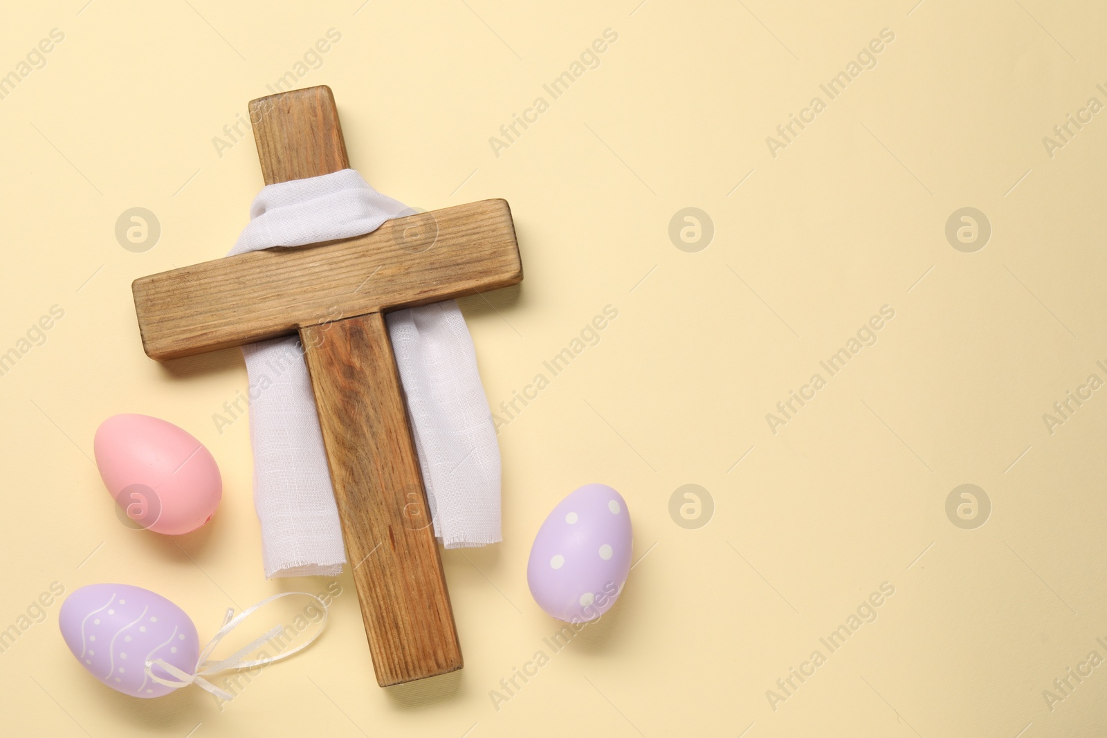 Photo of Wooden cross, white cloth and painted Easter eggs on beige background, flat lay. Space for text