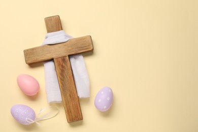 Wooden cross, white cloth and painted Easter eggs on beige background, flat lay. Space for text