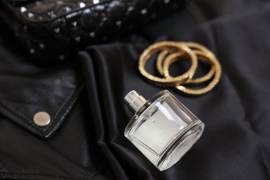 Photo of Leather bag, bottle of perfume and golden bracelets on black fabric, closeup