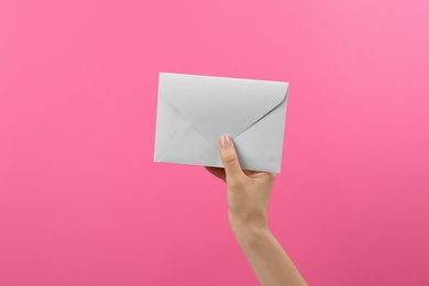 Photo of Woman holding white paper envelope on pink background, closeup