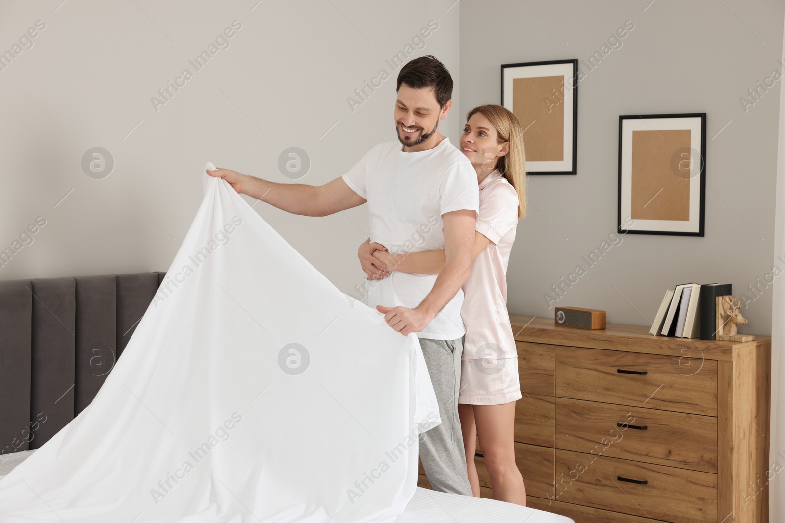 Photo of Couple changing bed linens in room. Domestic chores