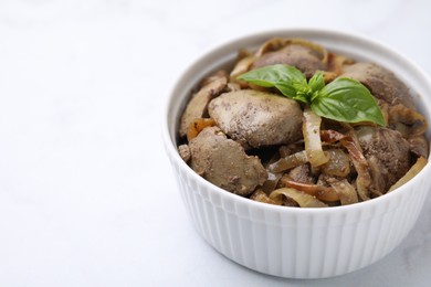 Photo of Delicious fried chicken liver with onion and basil in bowl on white table, closeup. Space for text