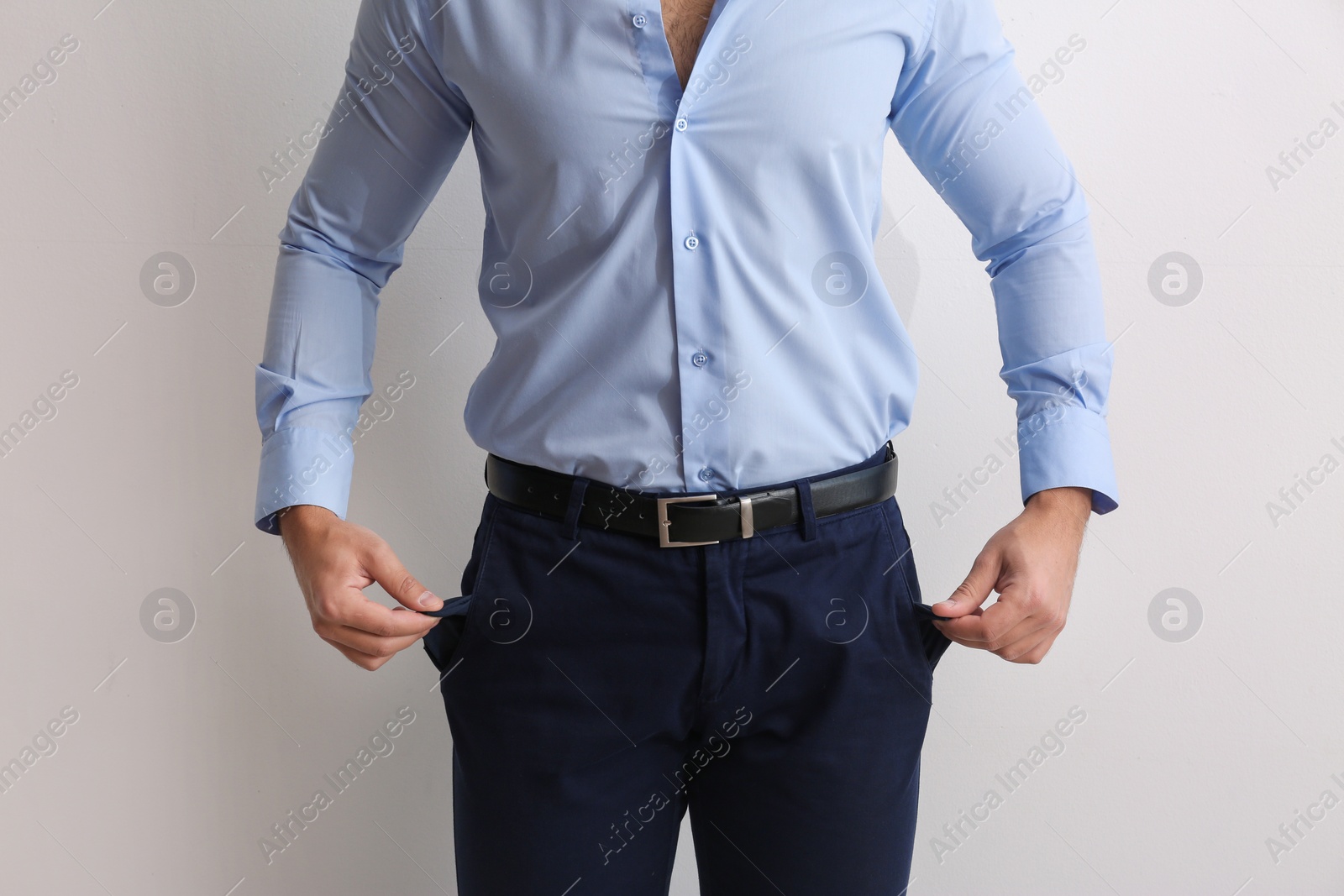 Photo of Businessman showing empty pockets on light background, closeup