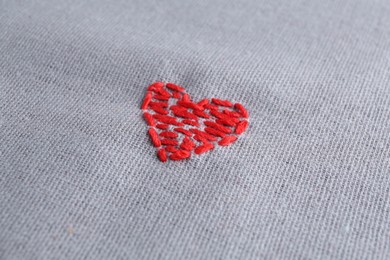 Photo of Embroidered red heart on gray cloth, closeup