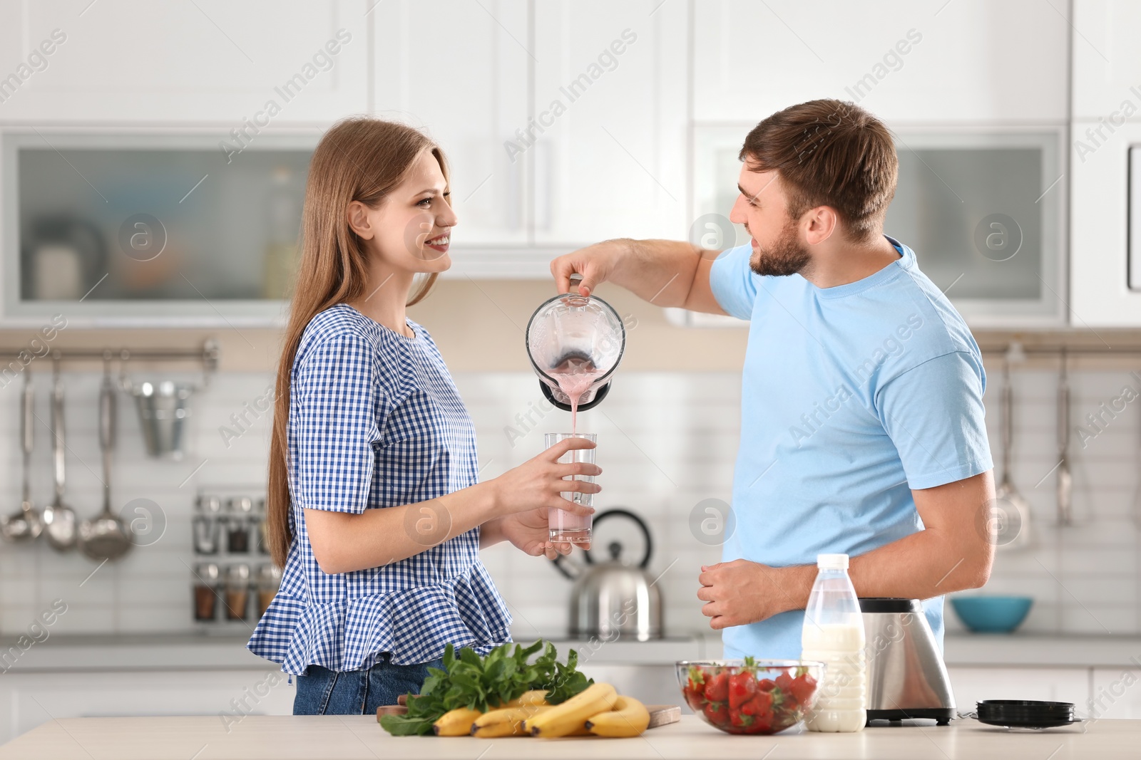 Photo of Young man pouring delicious milk shake into glass for his girlfriend in kitchen
