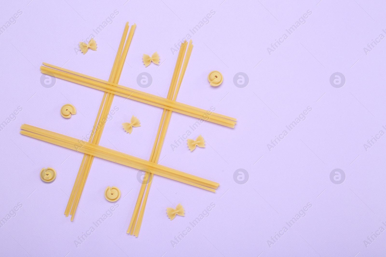 Photo of Tic tac toe game made with different types of pasta on lilac background, top view