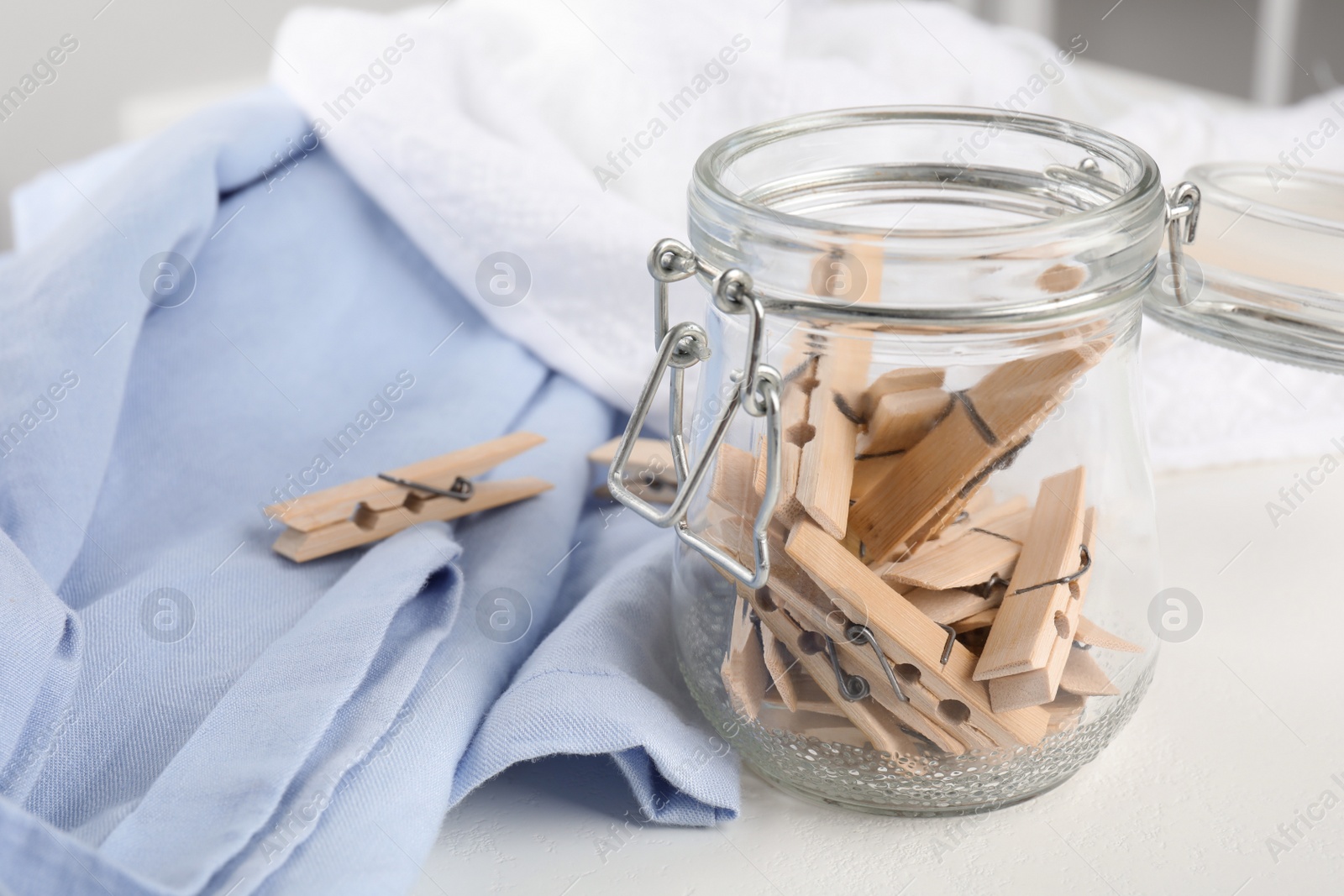 Photo of Many wooden clothespins in glass jar and fabric on white table