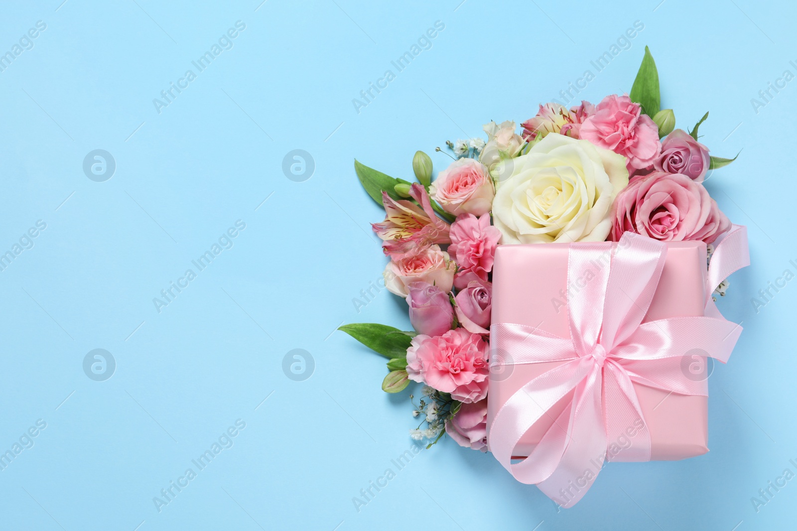 Photo of Gift box and beautiful flowers on light blue background, flat lay. Space for text