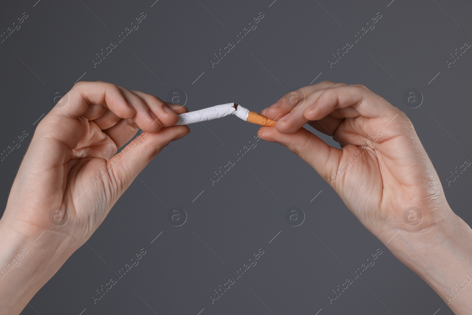 Photo of Stop smoking concept. Woman breaking cigarette on gray background, closeup