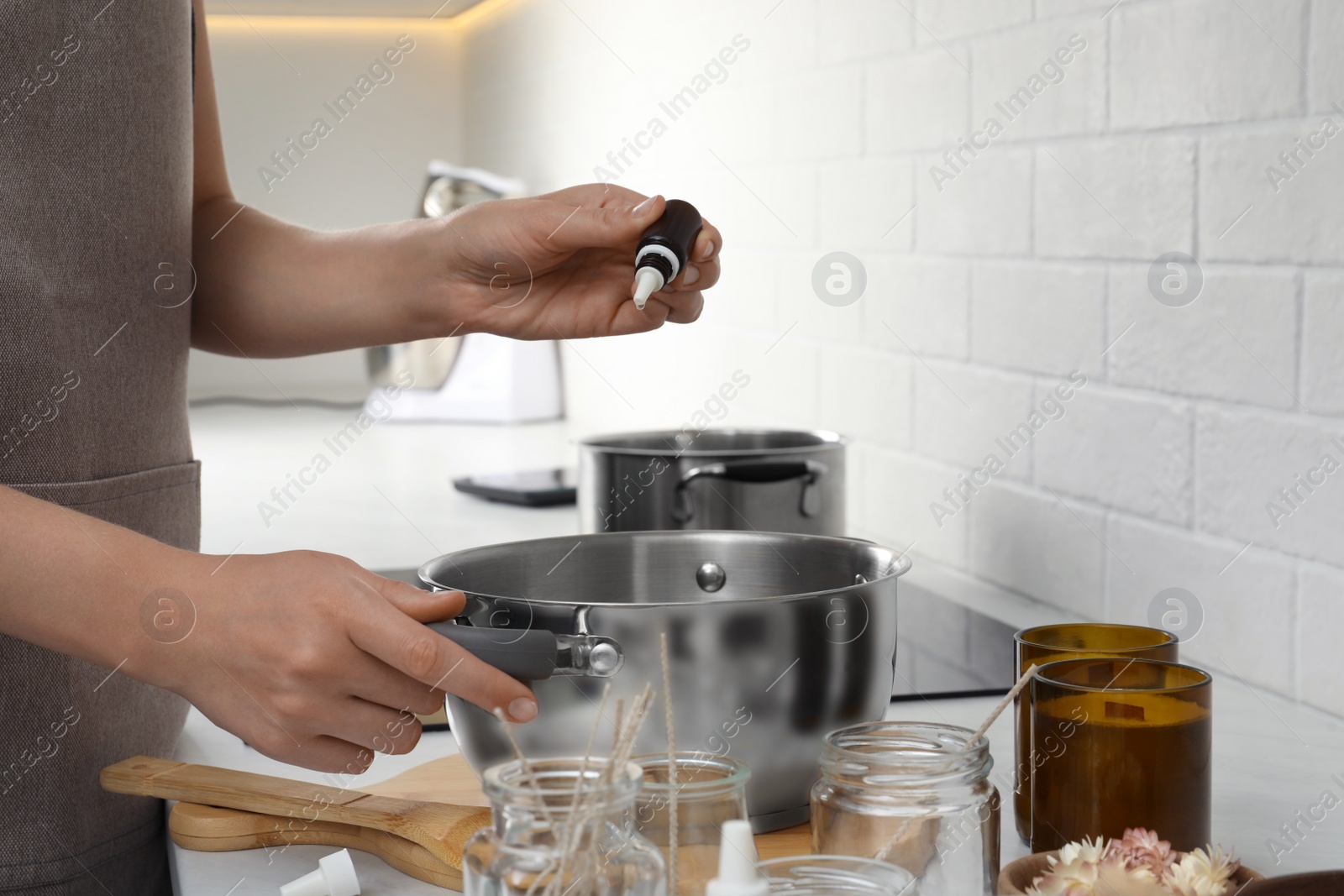 Photo of Woman adding essential oil into pot with melted wax at kitchen counter, closeup. Making homemade candles