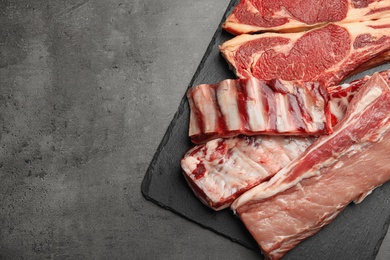 Slate plate with raw meat on grey table, flat lay. Space for text