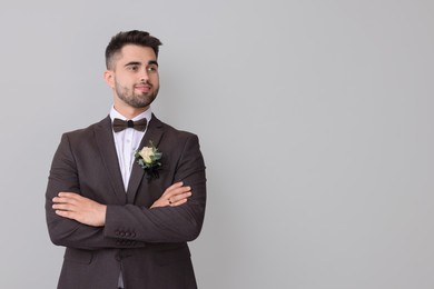 Photo of Handsome young groom with boutonniere on light grey background, space for text. Wedding accessory