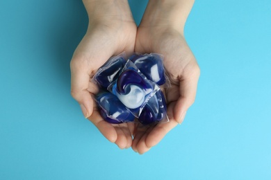 Photo of Woman holding laundry capsules on light blue background, top view