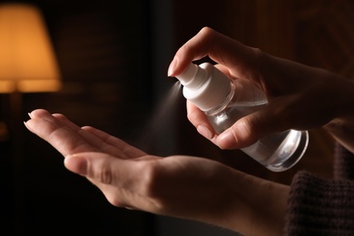 Woman spraying antiseptic onto hand against blurred background, closeup