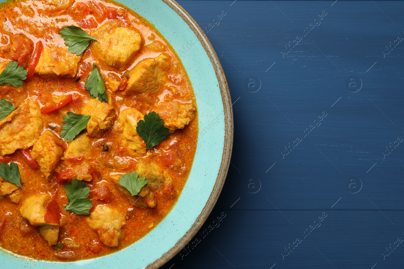 Photo of Delicious chicken curry on blue wooden table, top view. Space for text