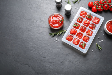 Ice cube tray with tomatoes, sauce and fresh rosemary on grey table, flat lay. Space for text