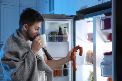 Photo of Young man taking sausages out of refrigerator at night