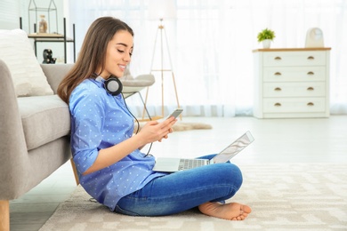 Photo of Attractive young woman with mobile phone on floor near sofa