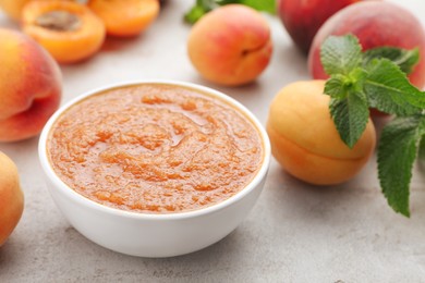 Photo of Apricot puree in bowl and fresh fruits on light grey table, closeup