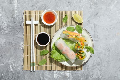 Photo of Tasty spring rolls served with sauces on grey textured table, top view