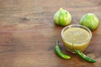 Photo of Tasty salsa sauce and ingredients on wooden table. Space for text