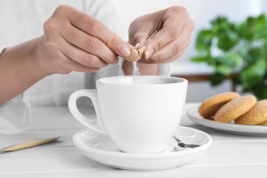 Woman adding sugar to aromatic coffee at white wooden table, closeup