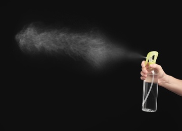 Woman spraying air freshener on black background, closeup