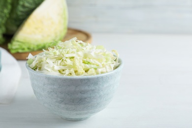 Photo of Cut fresh savoy cabbage in bowl on white wooden table
