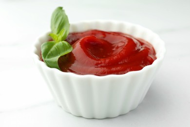 Bowl of tasty ketchup and basil on white marble table, closeup