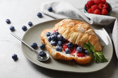 Photo of Delicious croissant with berries, almond flakes and spoon on light grey table
