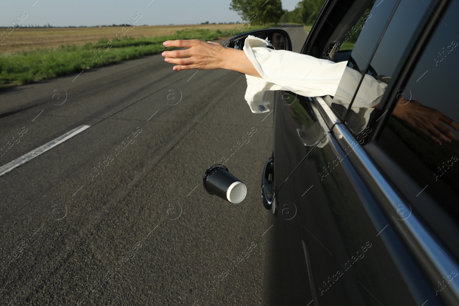 Photo of Driver throwing away paper cup from car window. Garbage on road