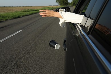 Driver throwing away paper cup from car window. Garbage on road